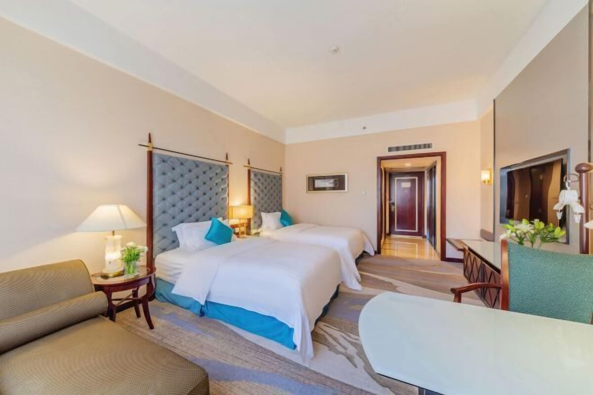 A hotel room with two beds, a sofa, a desk, and a mirror.