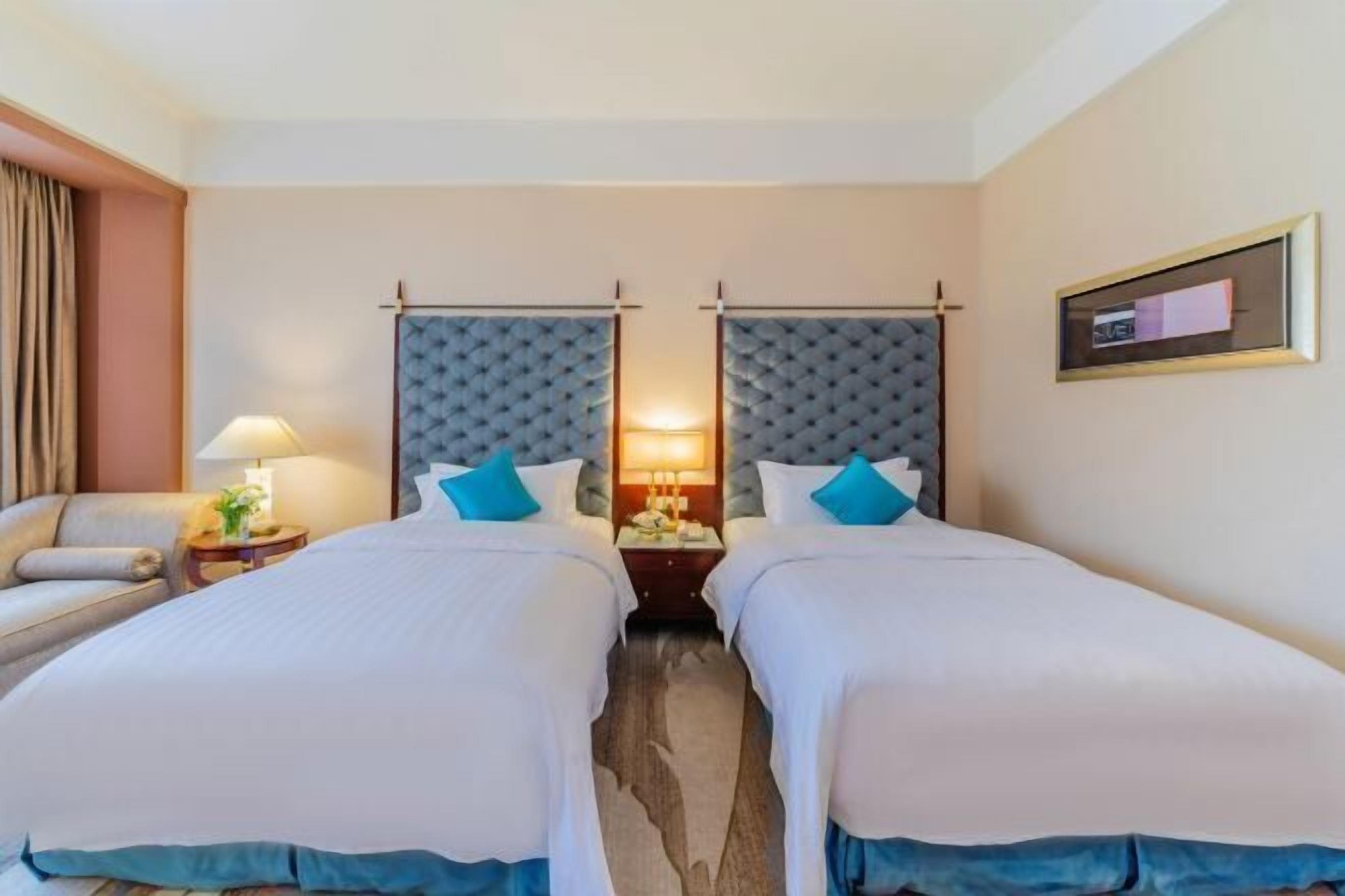 A hotel room with two beds, a nightstand with a lamp, and a framed picture on the wall.