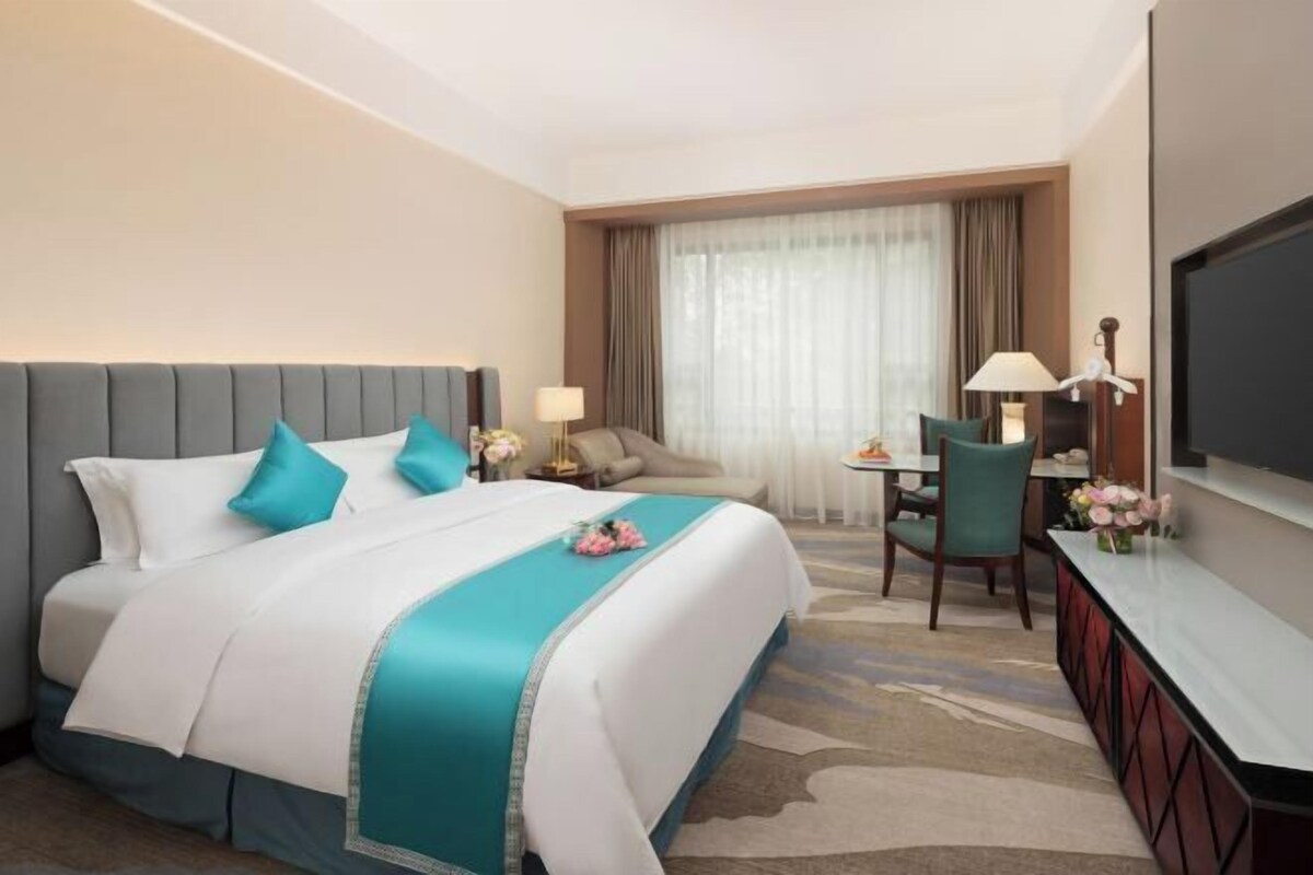 A hotel room with a bed, a desk, a chair, a TV, and a window with curtains.
