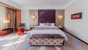 A hotel room with a large bed, a tufted headboard, a glass coffee table, a red ottoman, a nightstand with a lamp, and a framed picture on the wall. - Dongrong Hotel (Dongguan Municipal Government International Trade Center) (Dongguan)