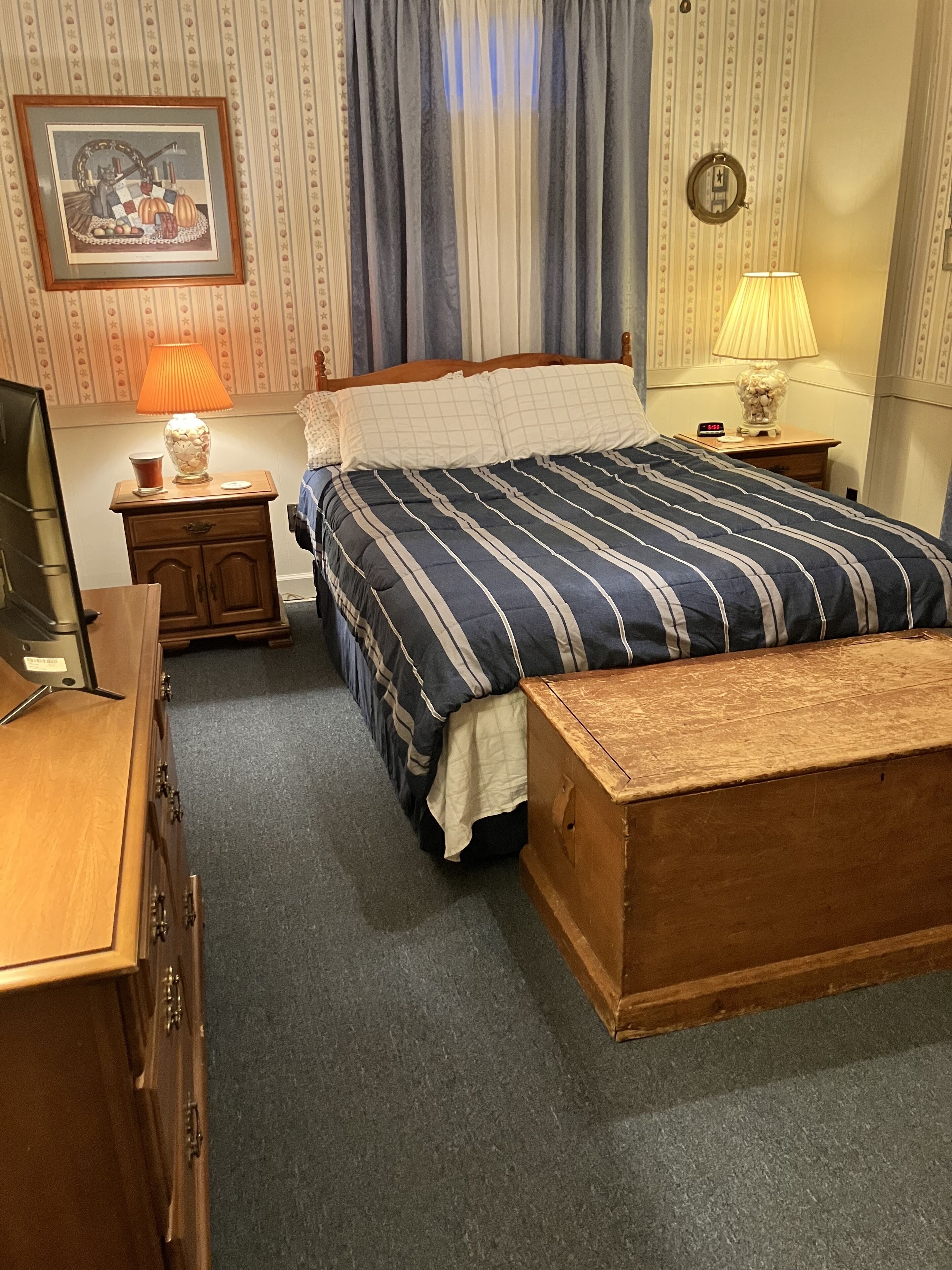 Un dormitorio ordenado con una cama grande, un aparador de madera, una mesita de noche con una lámpara y un cuadro en la pared.