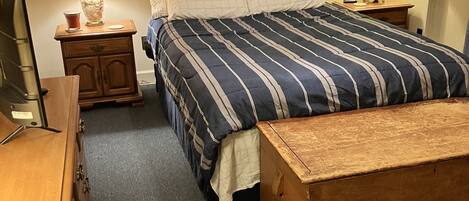 Un dormitorio ordenado con una cama grande, un aparador de madera, una mesita de noche con una lámpara y un cuadro en la pared.