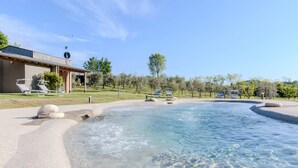 Une piscine de spa à l’eau claire, entourée d’une plage de galets et de chaises longues.