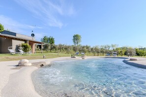 Een wellnesszwembad met helder water, omgeven door een kiezelstrand en ligbedden.