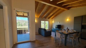 Un vaste espace de vie doté d’un plafond en bois, d’une table à manger pour quatre personnes, d’un canapé et d’un téléviseur.