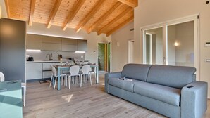 Un salon moderne avec un canapé gris, un plancher en bois et une cuisine en arrière-plan.