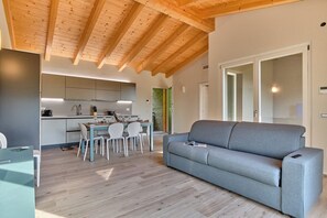 Een moderne woonkamer met een grijze bank, houten vloeren en een keuken op de achtergrond.