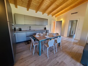 Une cuisine moderne avec des poutres en bois, une table à manger pour quatre personnes et une vue sur le salon attenant.