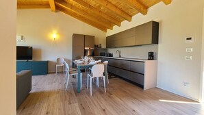 Une cuisine moderne avec des poutres en bois, un coin repas avec une table et des chaises, et un téléviseur posé sur un meuble.