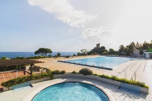 Ein Poolbereich mit Blick auf das Meer, einer Pergola und einer schlossähnlichen Struktur im Hintergrund.