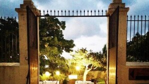 An outdoor dining area with tables and chairs, a stone-paved entrance, and a metal gate. - Allegroitalia Torre Artale Palermo (Trabia)