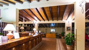 A reception area with a wooden reception desk, a tiled floor, and a high ceiling with exposed beams. - Allegroitalia Torre Artale Palermo (Trabia)