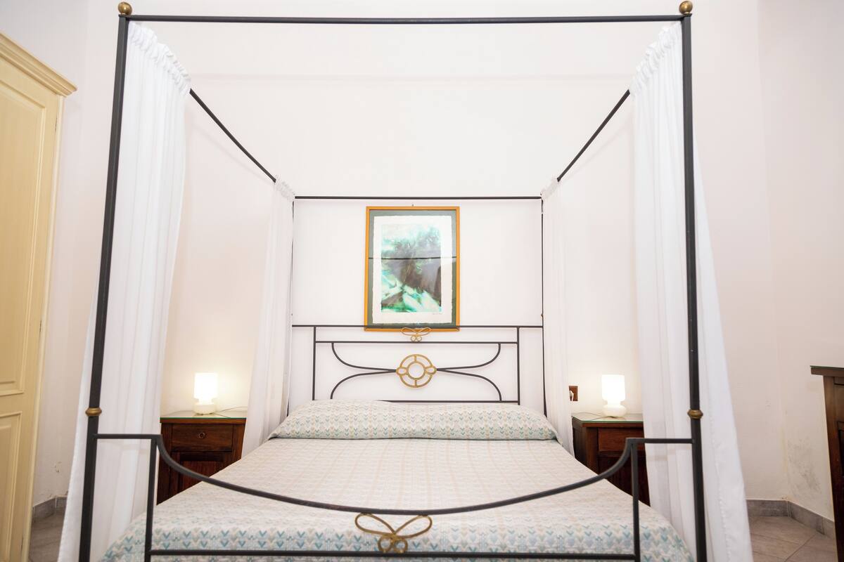 Una cama con dosel, una mesita de noche con lámpara y un cuadro enmarcado en la pared.