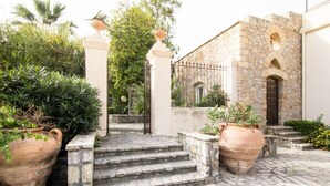 A courtyard with stone steps leading to a building with a stone facade and arched windows. There are large terracotta pots with plants on either side of the steps. - Allegroitalia Torre Artale Palermo (Trabia)