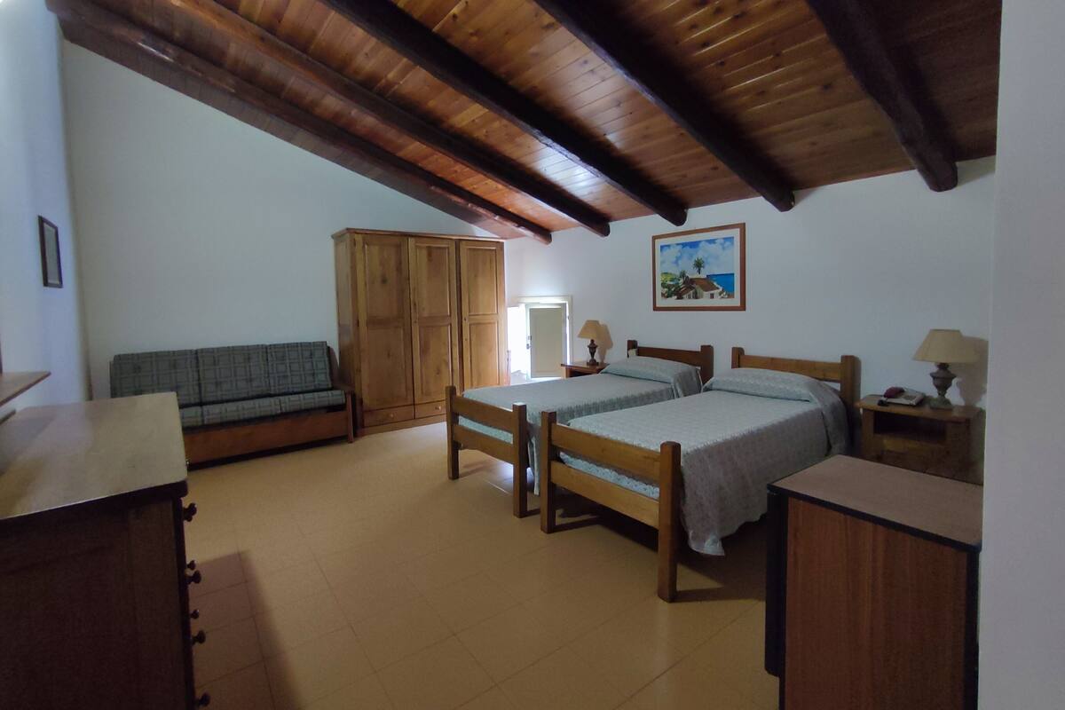 Una habitación con techo de madera, una cama, un sofá, un armario y un cuadro en la pared.