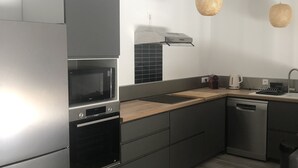 A modern kitchen with grey cabinetry, a wooden countertop, a built-in oven, a microwave, a dishwasher, and two hanging wicker pendant lights. - Villa 10 minutes from the quiet beach (Soulac-sur-Mer)