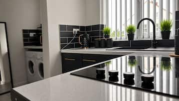 Una cocina moderna con una isla grande, baldosas blanco y negro, lavadora y plantas en macetas.
