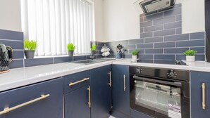 A modern kitchen with dark blue cabinets, a white countertop, and a built-in oven. - The Annexe, 25 Gorsehill Road (Wirral)