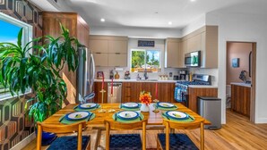 A modern kitchen with wooden cabinets, a stainless steel refrigerator, and a dining area with a wooden table set for four.