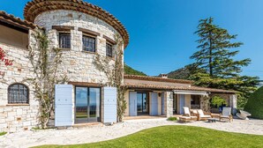 Un edificio in pietra con facciata curva, ampie finestre e una terrazza con posti a sedere all'aperto.
