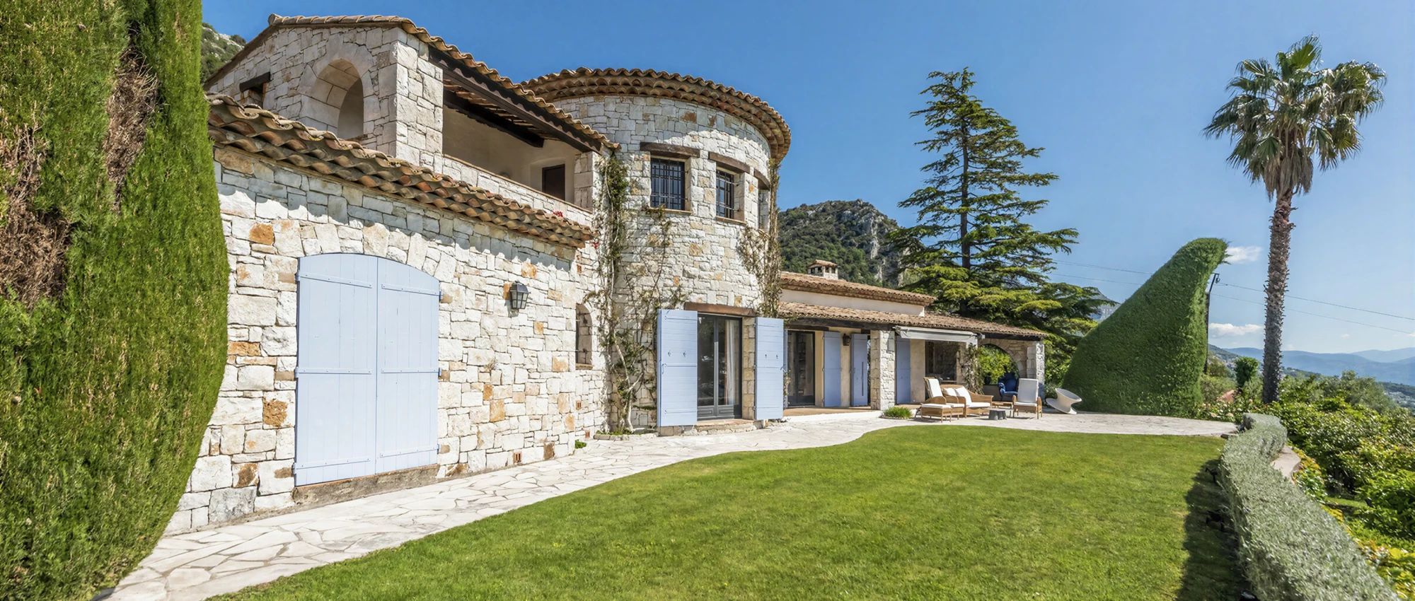 A stone building with a curved roof, a paved driveway, and a well-maintained lawn.