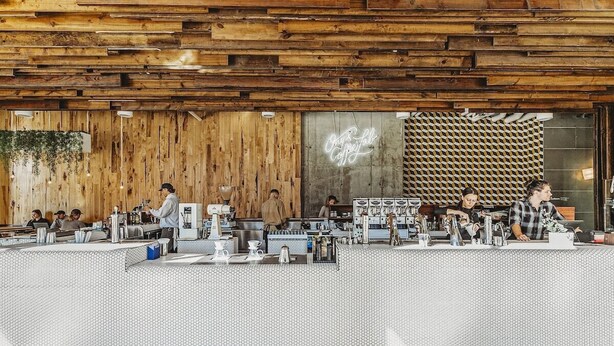 Un café con interior de madera, un letrero de neón y una barra con varios equipos para preparar café.