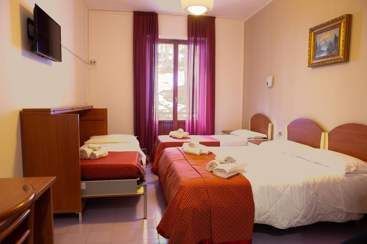 A hotel room with two single beds, a double bed, a TV mounted on the wall, and a painting on the wall.