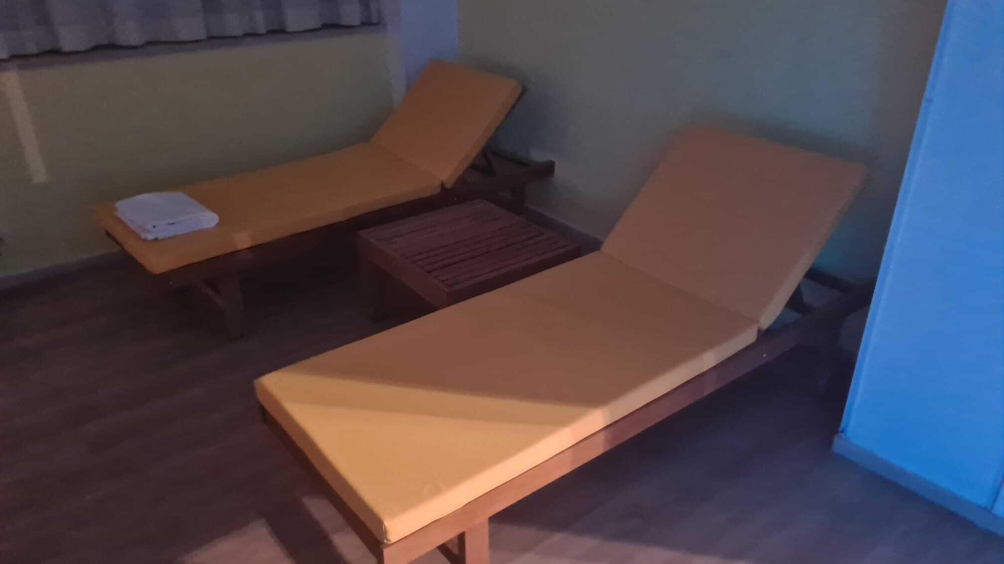Una habitación con dos sillones de madera, uno con una toalla encima, y una pequeña mesa de madera.
