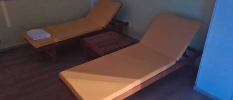 Una habitación con dos sillones de madera, uno con una toalla encima, y una pequeña mesa de madera.