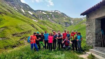 Un grupo de personas de pie en una zona montañosa con un edificio de piedra en primer plano.