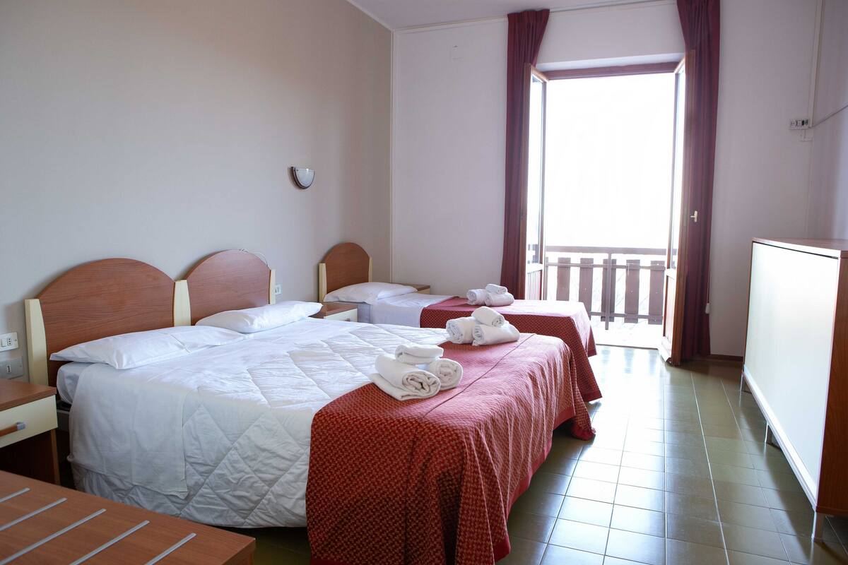 A hotel room with two beds, a desk, and a balcony.