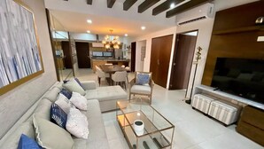 A modern living room with a sofa, coffee table, and a TV. There is a dining area with chairs and a table. - Moderno departamento con alberca, 200m al malecón (Mazatlán)