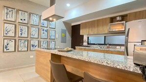 A modern kitchen with a central island, two bar stools, and framed botanical artwork on the wall. - Moderno departamento con alberca, 200m al malecón (Mazatlán)