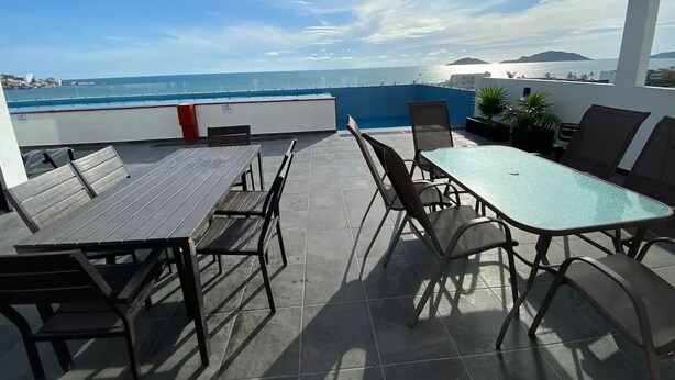 A terrace with a view of the sea, featuring a table and chairs, and a blue railing. - Moderno departamento con alberca, 200m al malecón (Mazatlán)