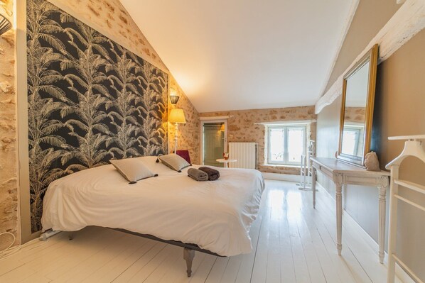 A bedroom with a large bed, a nightstand, a mirror, and a window.