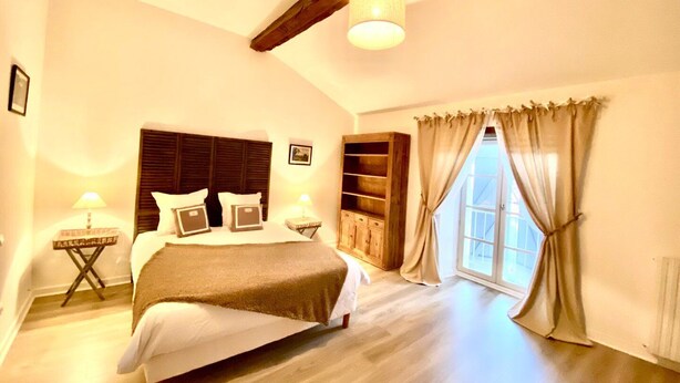 Ein Schlafzimmer mit einem großen Bett, einem Holzkopfende, Nachttischen, einem eingebauten Kleiderschrank und einem Fenster mit Vorhängen.