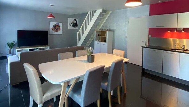 A modern kitchen with a red backsplash, a dining area with a white table and grey chairs, and a staircase leading to a loft.