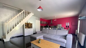 A modern living room with a grey sofa, a wooden coffee table, and a staircase leading to a kitchen area.