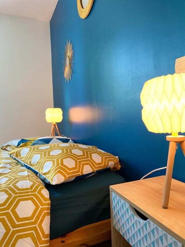 A bedroom with a bed, two bedside lamps, a wall clock, and a storage unit.