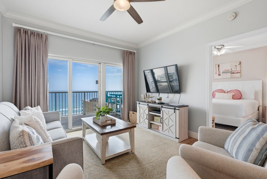 A living room with a sofa, a coffee table, a TV, and a balcony with a view.
