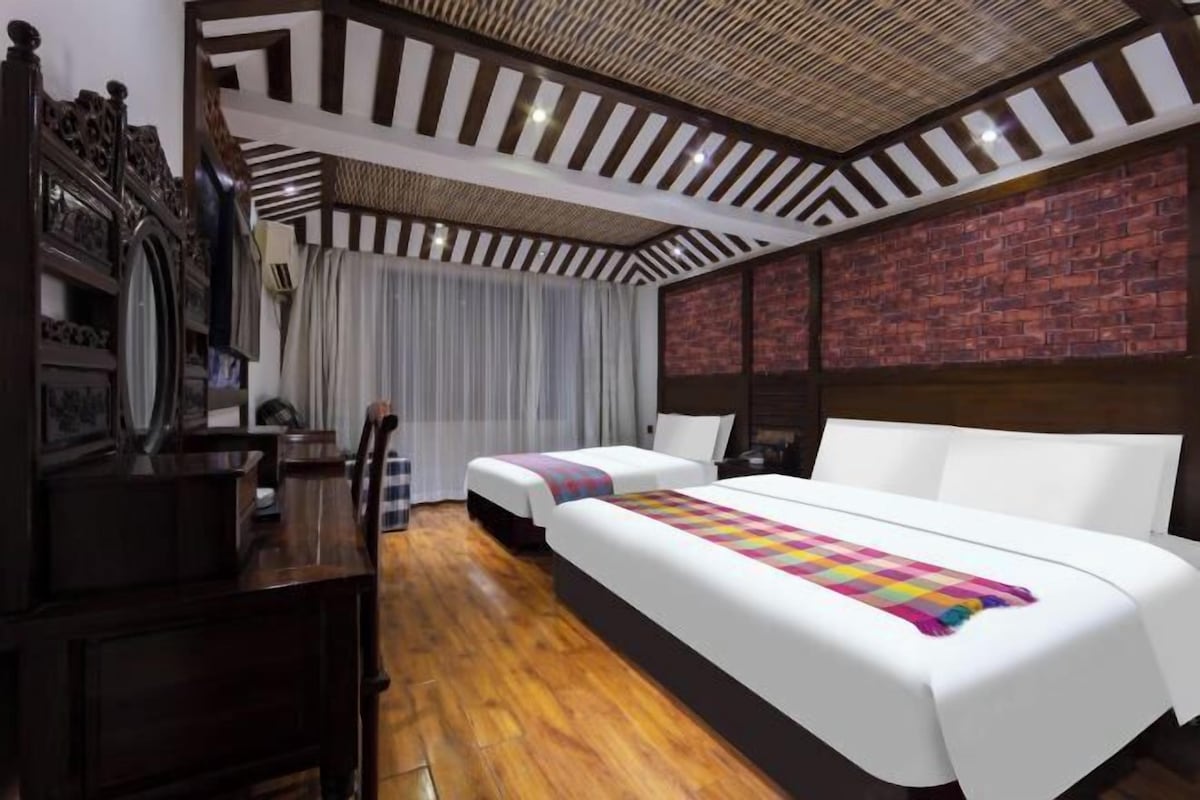 Ein Hotelzimmer mit Holzboden, zwei Betten mit weißer Bettwäsche, einer Wand aus Ziegelsteinen und einer Decke mit Holzbalken.