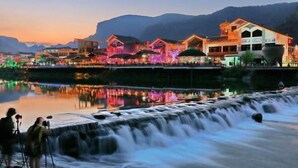A hotel with a waterfall feature in front, surrounded by colorful lights and a mountainous backdrop. - Zhangjiajie Wulingju Inn (Wulingyuan Scenic Area) (Zhangjiajie)