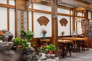 Een klassiek interieur met houten balken, een waterpartij van steen en een eetgedeelte met tafels en stoelen.