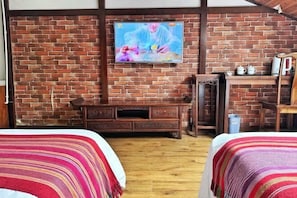 Ein Zimmer mit Backsteinwand, einem an einer Holzkabine montierten Fernseher und zwei Betten mit gestreifter Bettwäsche.