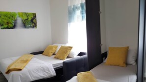 Two single beds with white linens and yellow towels, a dark-colored sofa, and a painting of a bridge. - Apartment Prijeboj 2 - Plitvice Lakes 6km from apartment (Prijeboj)