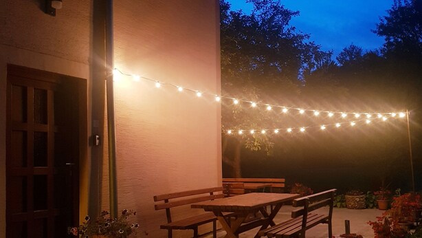 A patio with a wooden table and benches, string lights, and potted plants. - Apartment Prijeboj 2 - Plitvice Lakes 6km from apartment (Prijeboj)