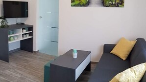 A modern living room with a dark sofa, a coffee table, a flat-screen TV, a bookshelf, and a painting of a forest pathway. - Apartment Prijeboj 2 - Plitvice Lakes 6km from apartment (Prijeboj)