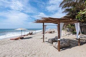 A beach with wooden cabanas, lounge chairs, and a sandy beach. - KiChic (Máncora)