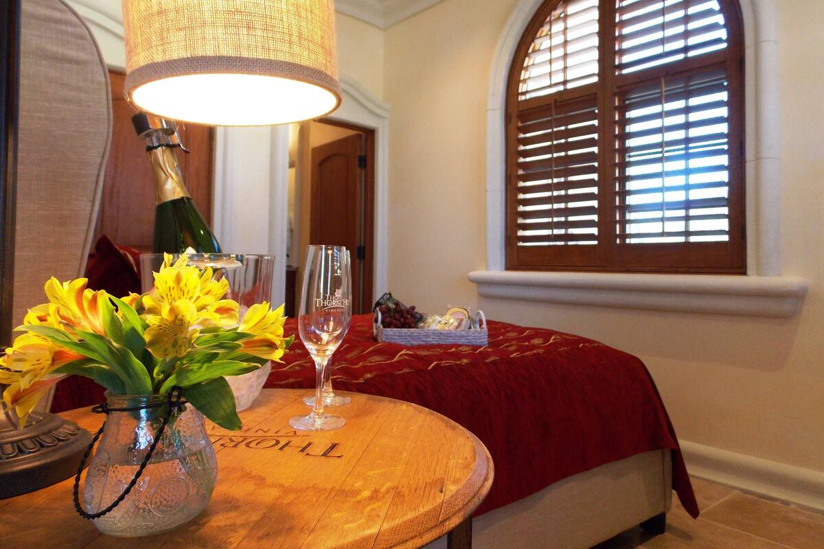 A room with a wooden table, a vase with yellow flowers, a bottle of champagne, and a glass.