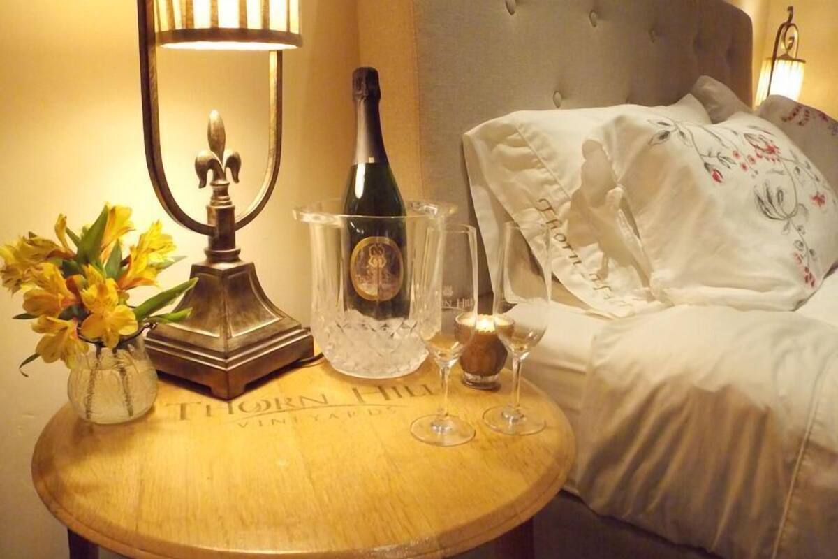 A round wooden table with a bottle of champagne, a candle, and a vase of yellow flowers.